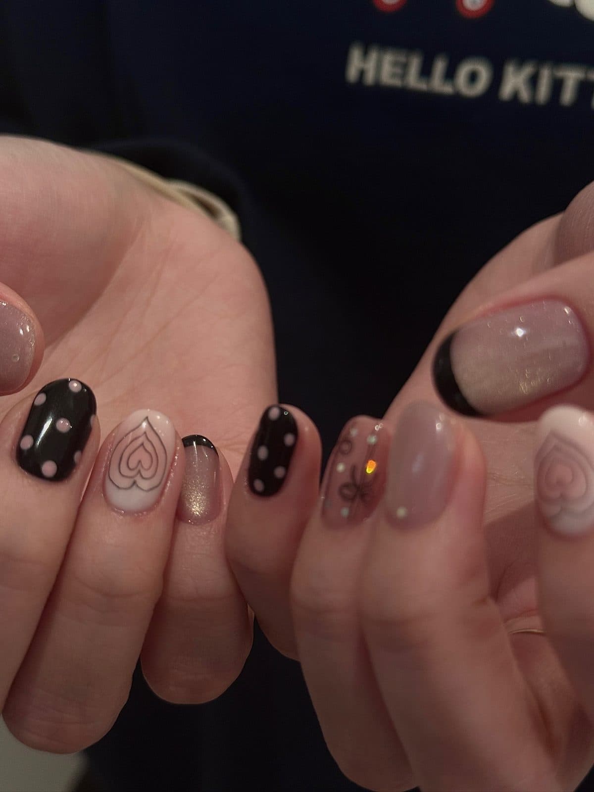 Short gel nails in black with white dots, heart outlines and a ribbon at Joy Nail Studio Vancouver