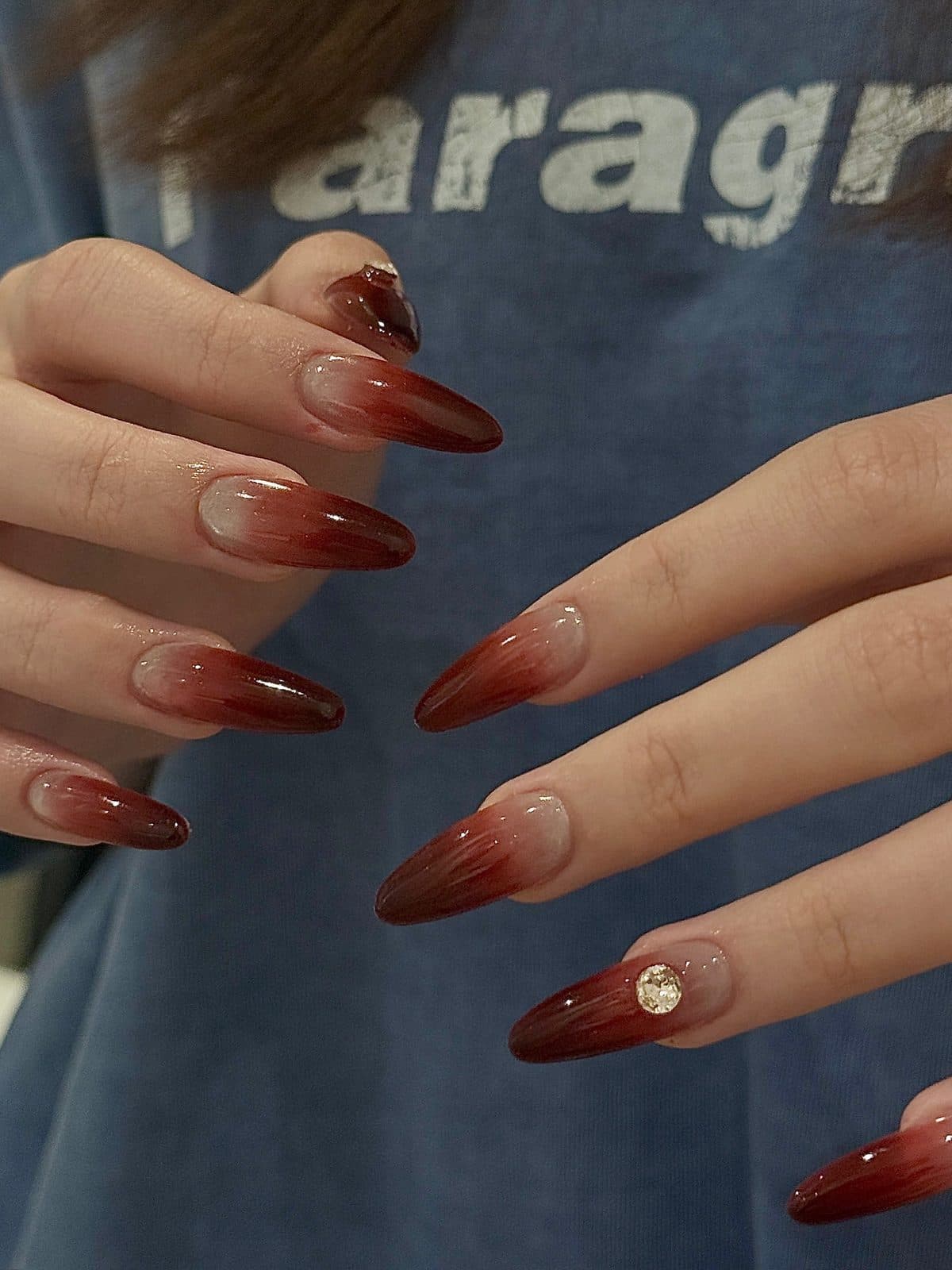 Long stiletto gel extensions in a deep burgundy ombre with a crystal accent at Joy Nail Studio Vancouver