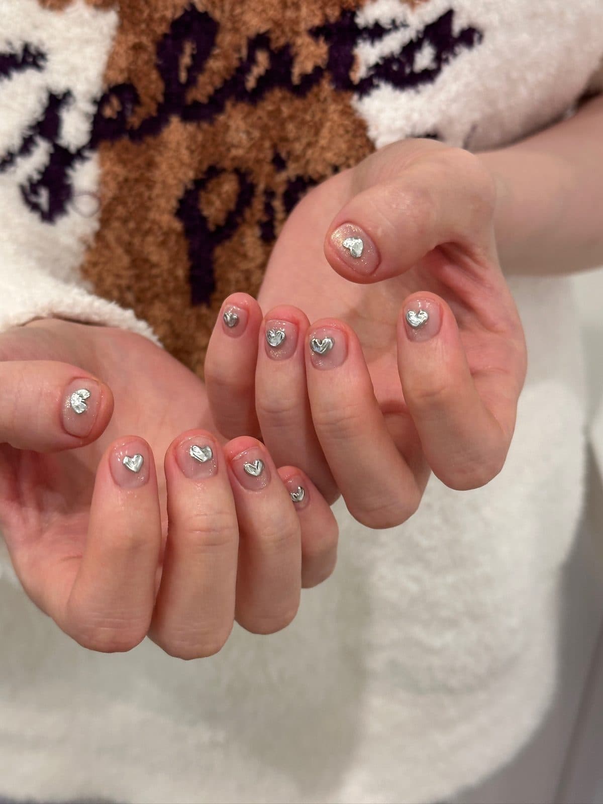 Short gel nails in sheer nude with tiny silver heart studs at Joy Nail Studio Vancouver