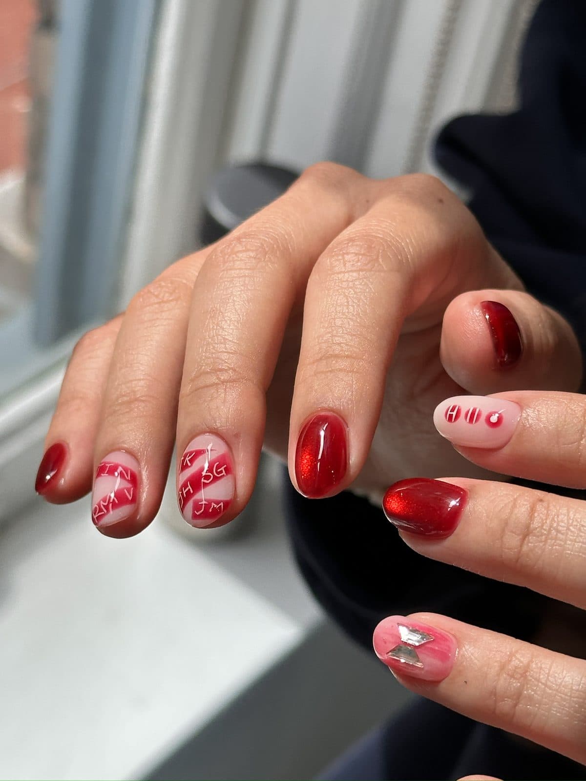 Short gel nails in red cat-eye gel with hand-painted lettering at Joy Nail Studio Vancouver
