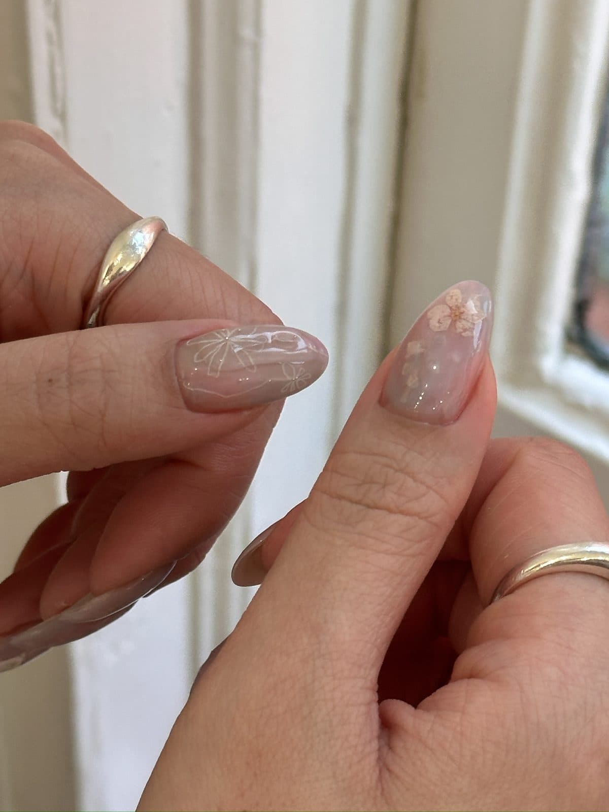 Close-up of a fine bow and flower drawn on a sheer nude gel nail at Joy Nail Studio Vancouver