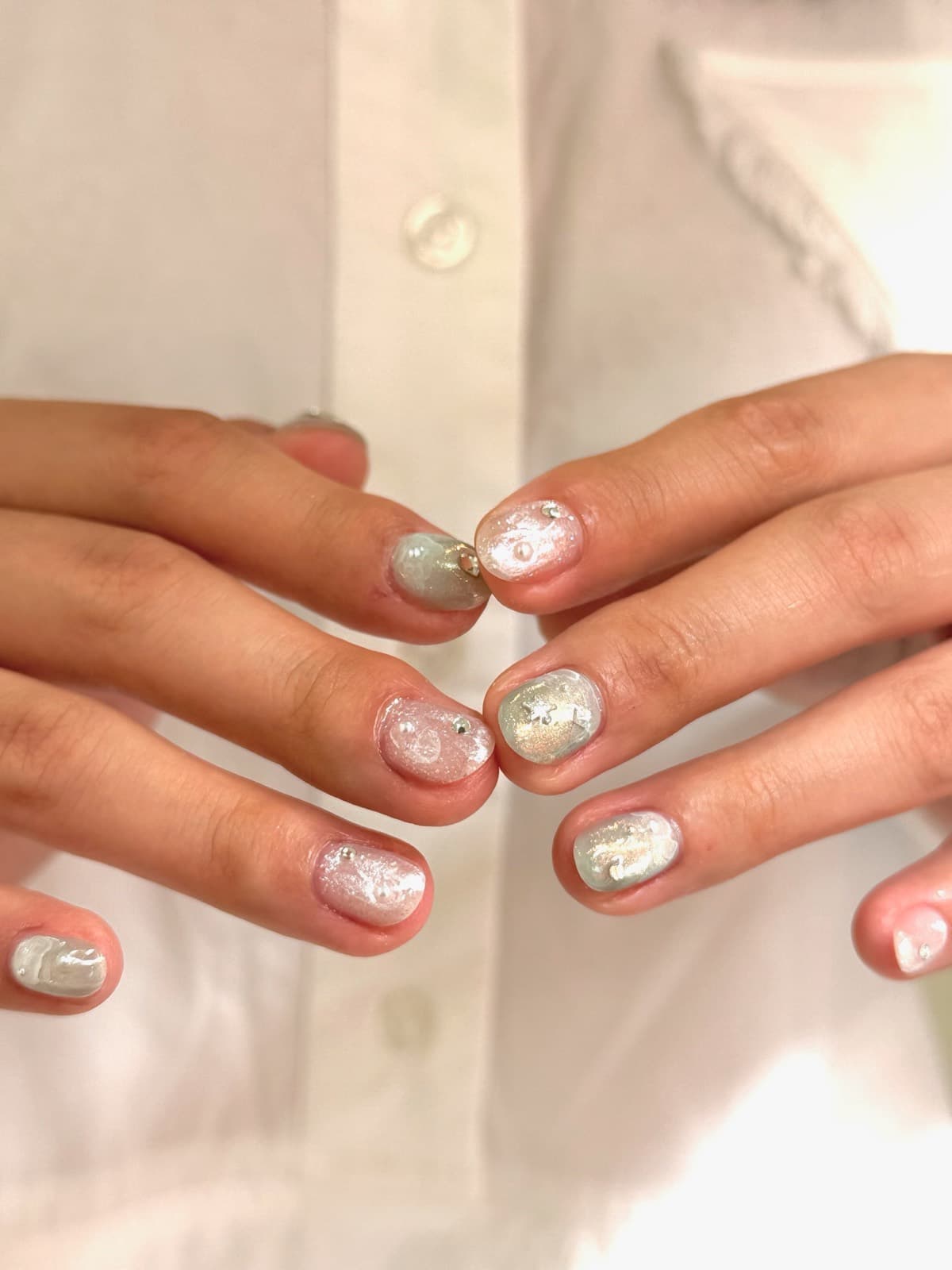 Short round Korean gel nails in sheer pink and sage green with pearl shimmer, small crystals and a star accent, by Joy Nail Studio Vancouver