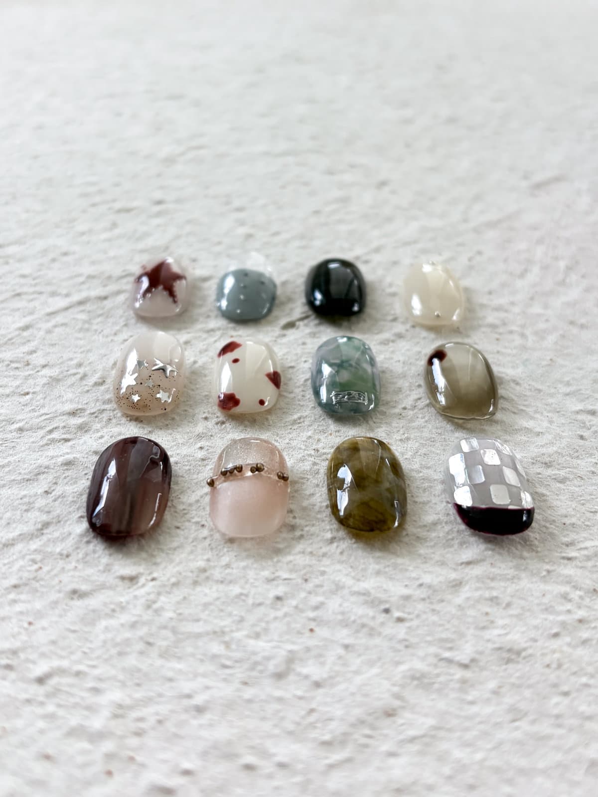 Twelve September nail art sample tips on a white plaster tray — burgundy star and spot designs, olive, tortoiseshell, moss marble, grey checker and pearl-stud accents by Joy Nail Studio Vancouver