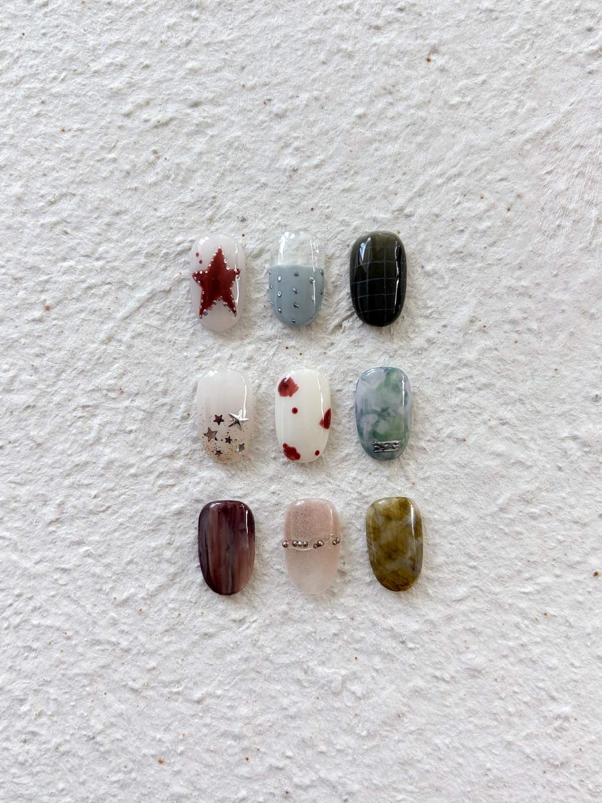 Nine September nail art sample tips in a grid — red star on nude, dusty blue dots, dark green, silver stars, burgundy spots on cream, green marble with a metal charm, burgundy marble, gold beads and tortoiseshell by Joy Nail Studio Vancouver