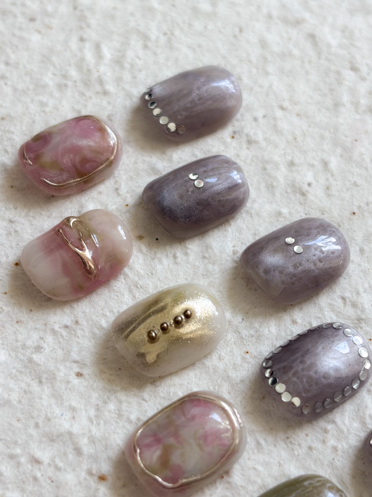 Close-up of September nail art sample tips in pink marble and greige with rows of pearl studs and one gold-foil nail by Joy Nail Studio Vancouver